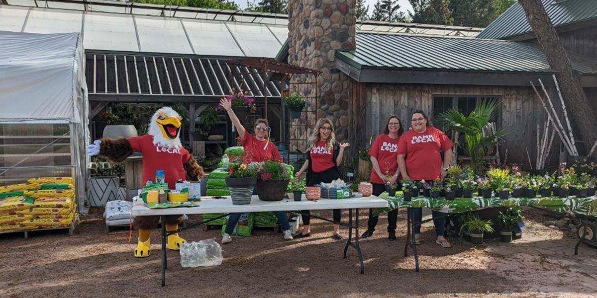 First National Bank employees pose in front of Oakridge Nursery in Brandon. A table is covered with plants to be given away.