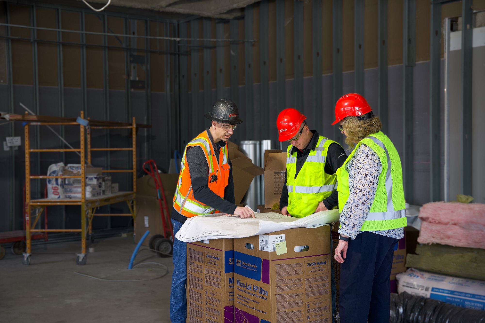 Kae Klinkenborg looks at blueprints with two male construction workers in a room under remodel.