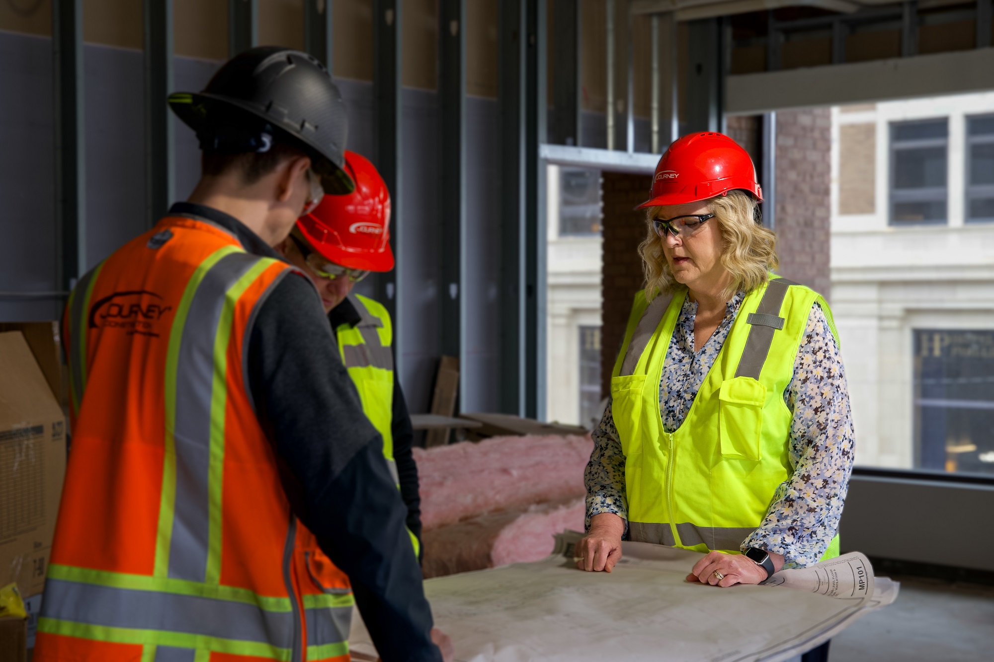 Kae Klinkenborg discusses blueprints with two male construction workers in a room under remodel.