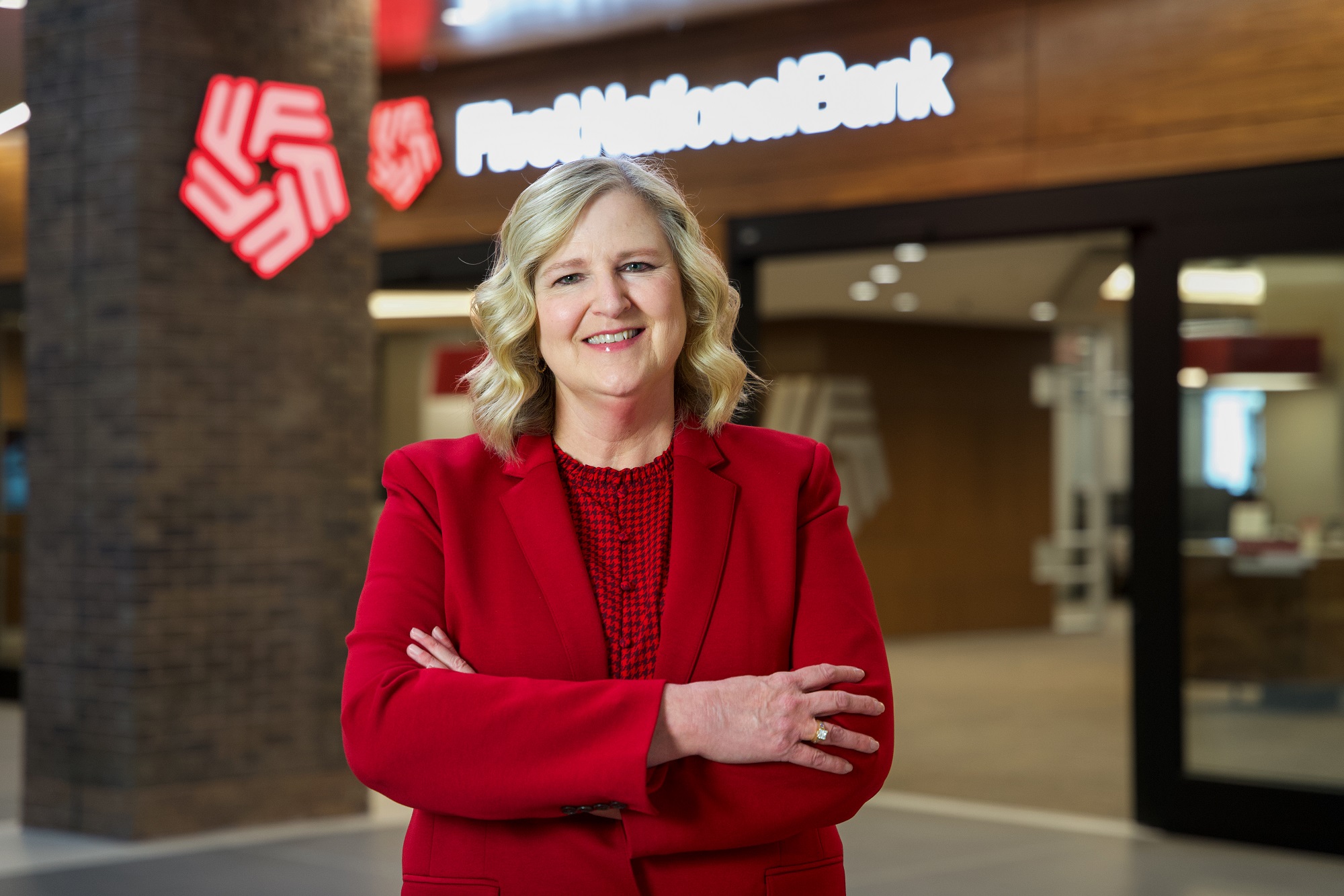 Kae Klinkenborg stands in front of a First National Bank sign in the Bank's Downtown atrium.