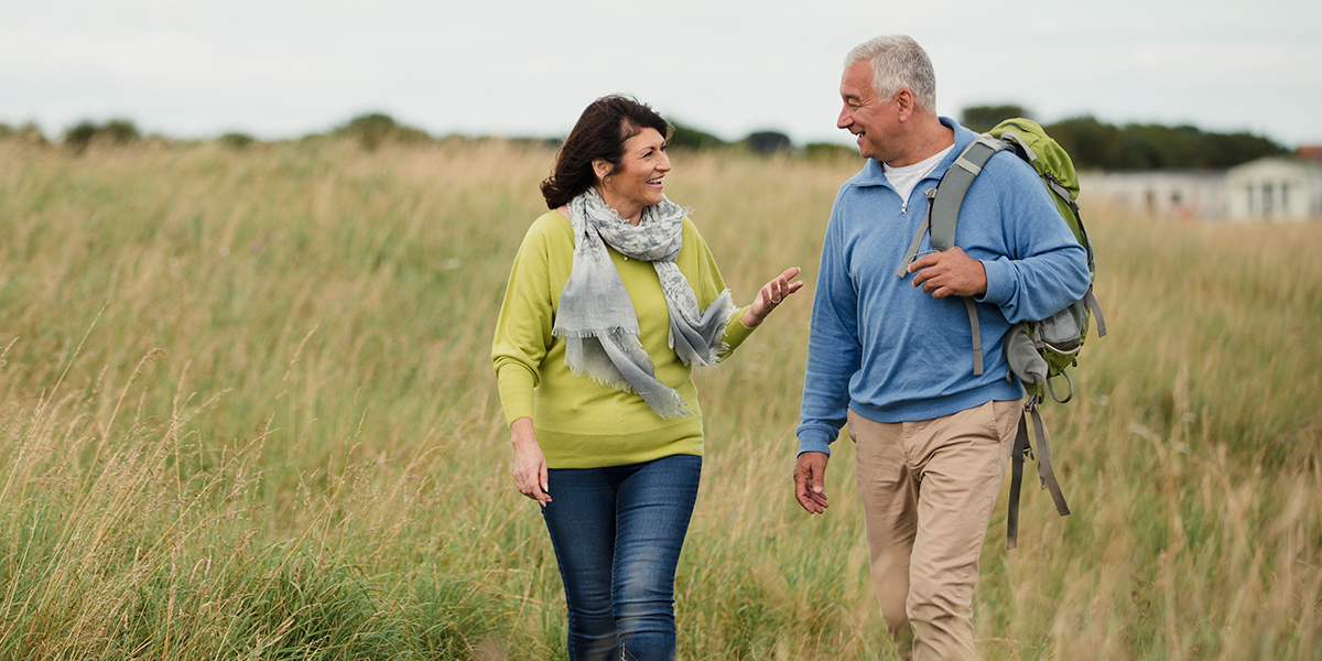 A middle-aged couple enjoying retirement by hiking a grassy trail. 