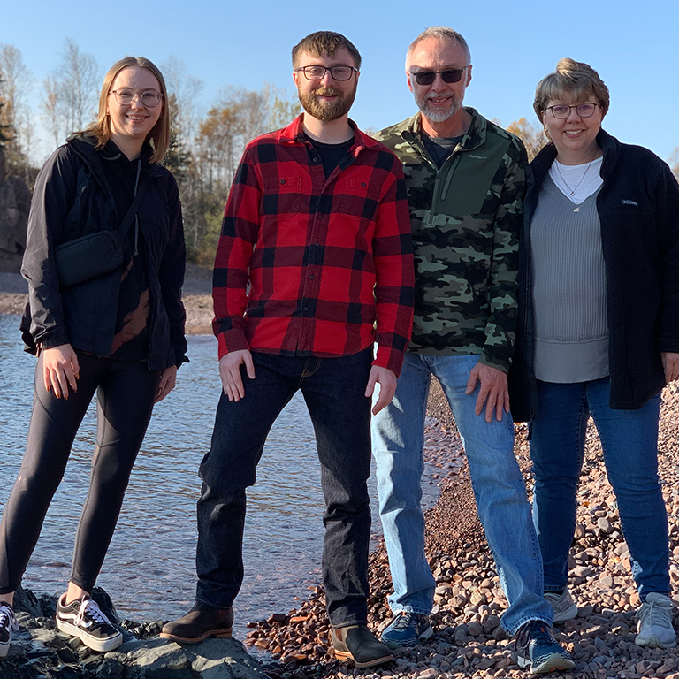 Lisa Hochhalter and her family pose for a picture near a body of water at the bottom of a rocky cliff.