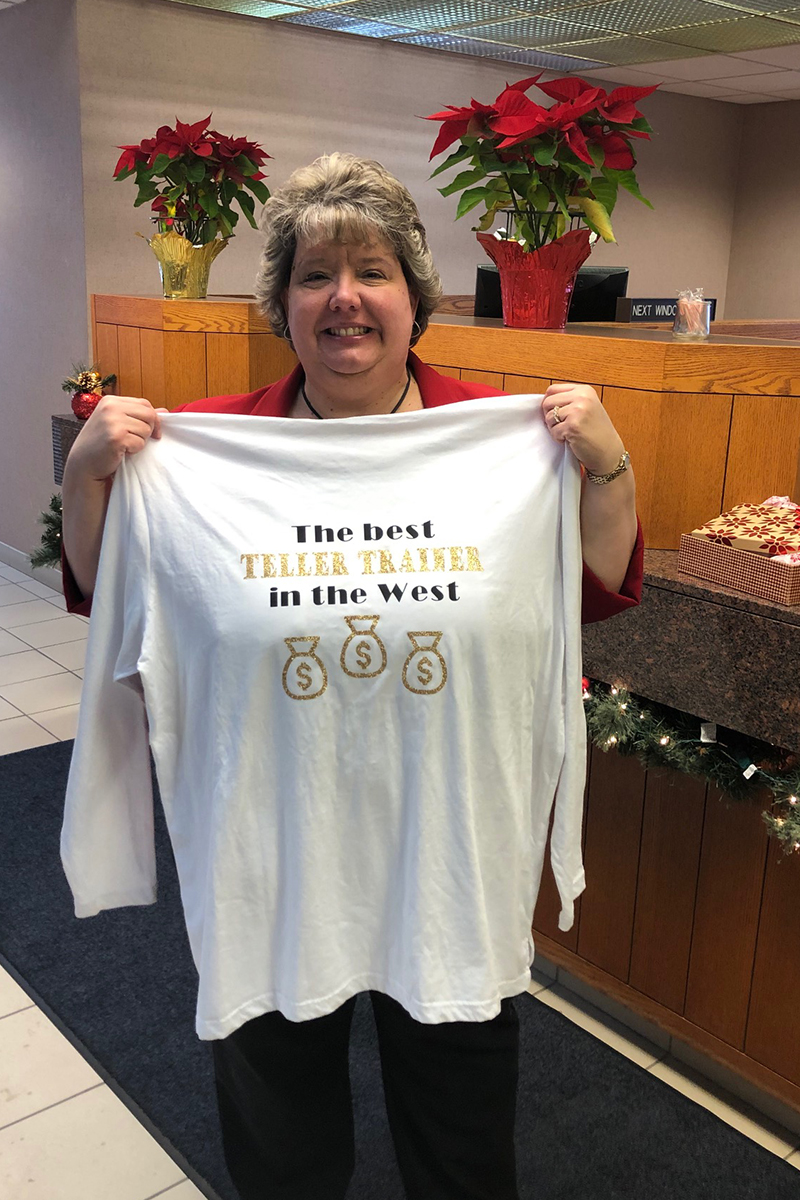 Sally Chapman holding a t-shirt that reads, "The best Teller Trainer in the West."
