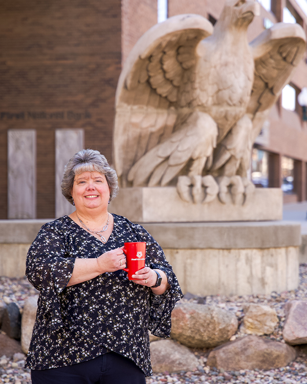 Sally Chapman poses in front of an eagle statue while holding a mug for her Tea With Teammates "mug shot."
