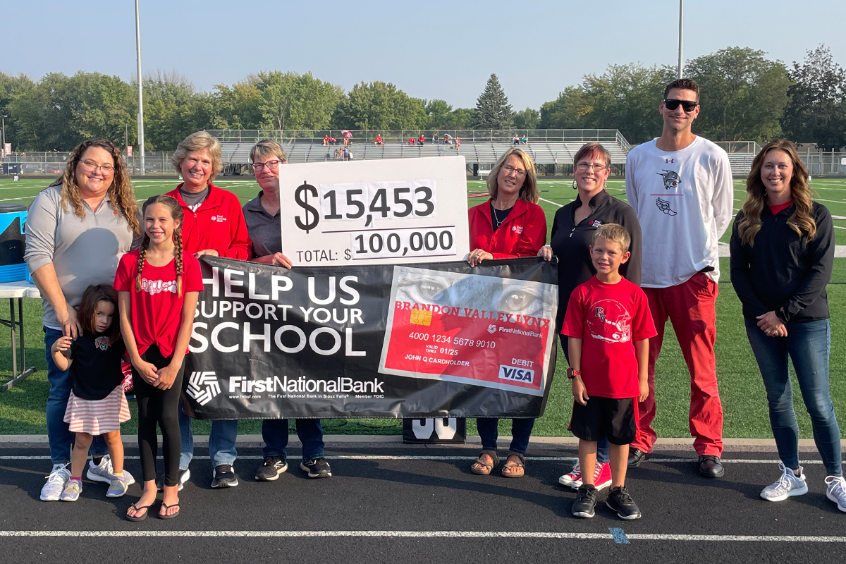 A group of people hold a Community Card banner and large check at Brandon Valley's check distribution.