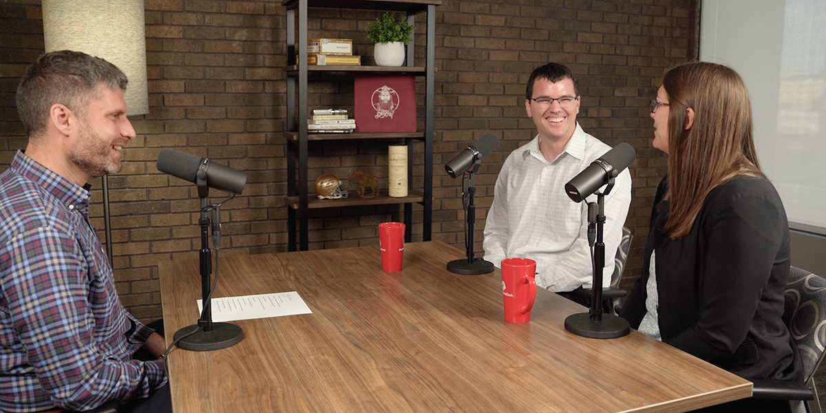 Brittany and Josh Evans sit at a table with Adam Cox to record a podcast episode.