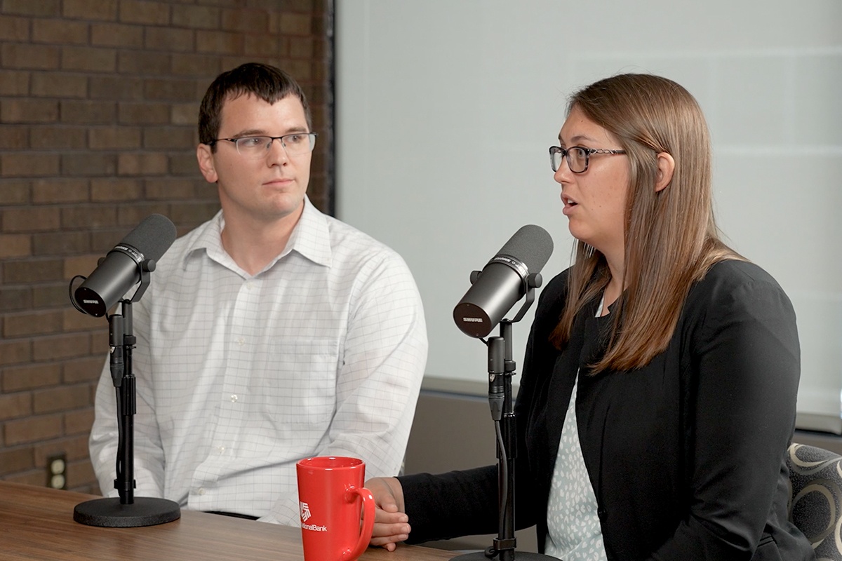 Brittany and Josh Evans sit in front of microphones to record their podcast episode, "How We Money: Knocking Out Debt."