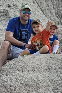 Seth Peterson poses for a picture with his two sons while hiking on a rock formation.
