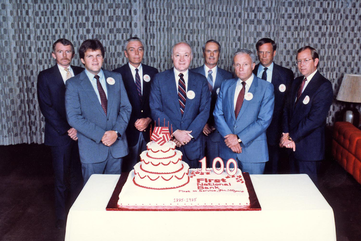 First National Bank's leadership team celebrating 100 years in business with a large cake. 