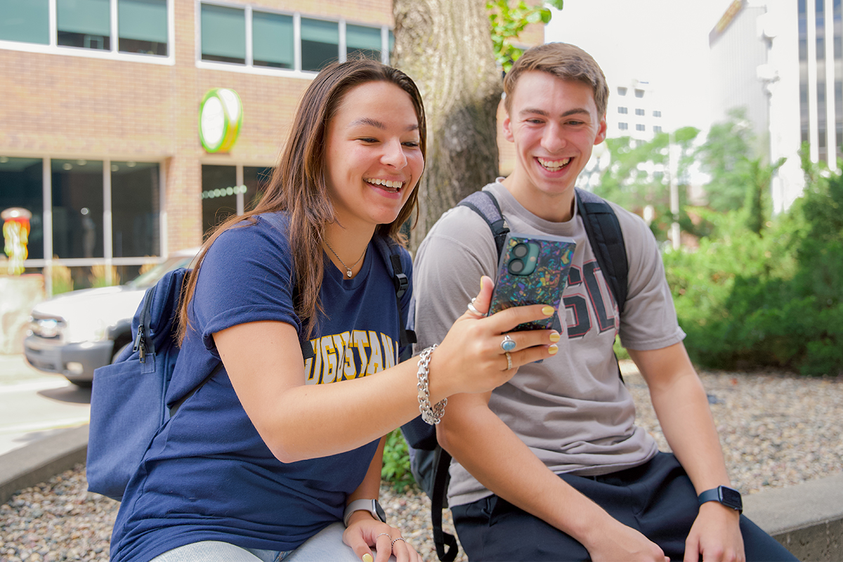 A teenage girl showing something on her phone to a teenage boy.