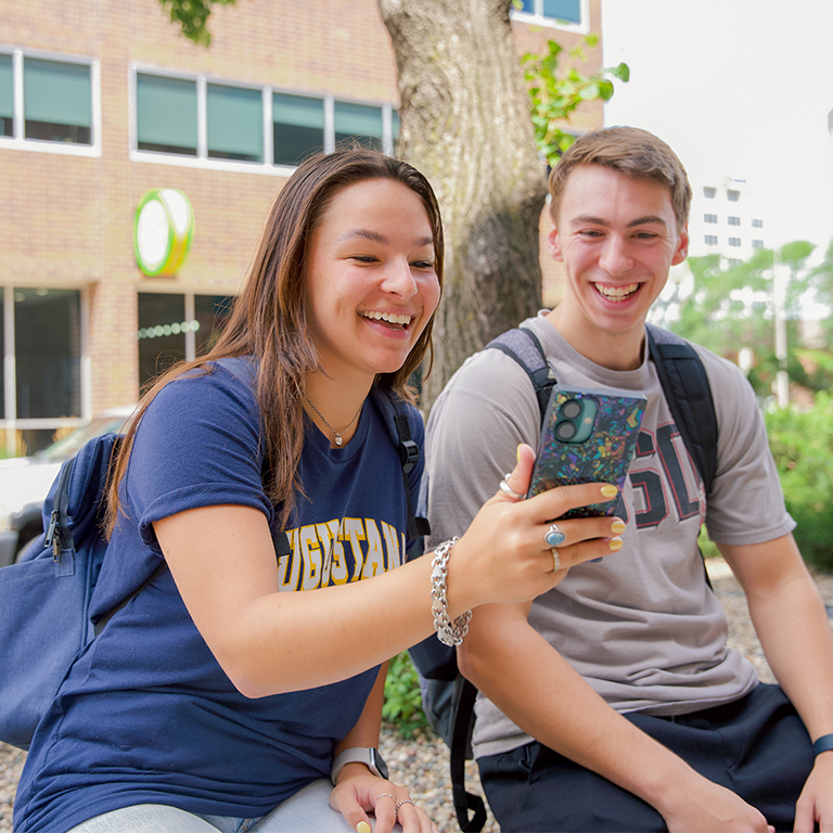 A teenage girl showing something on her phone to a teenage boy.