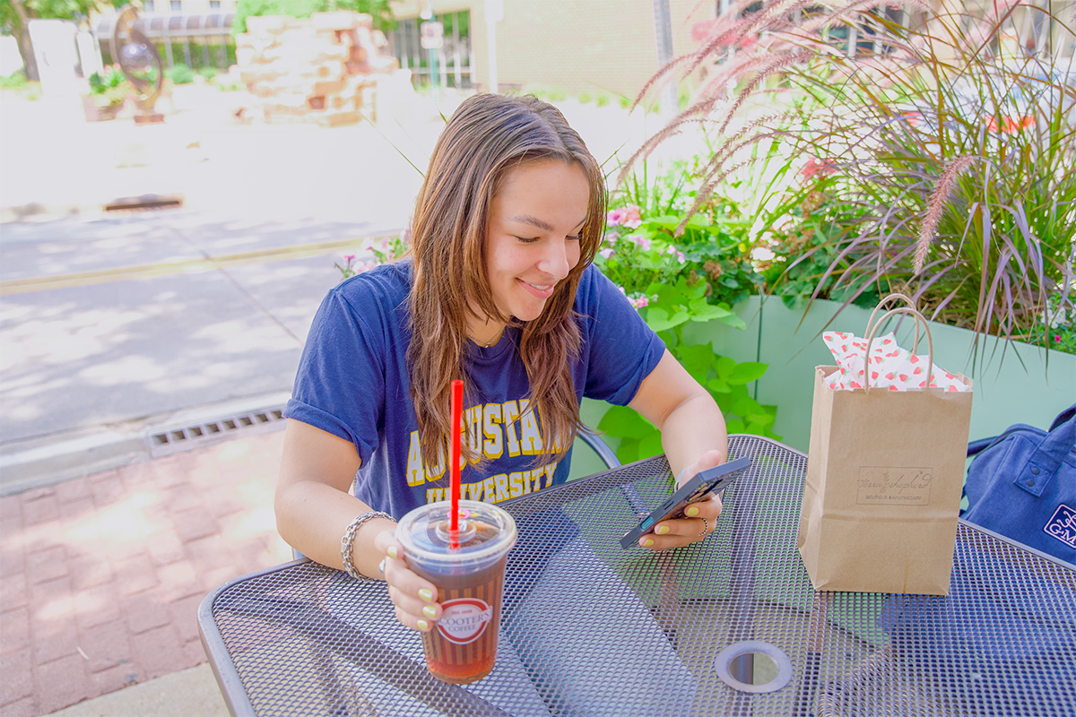 A teenage girl scrolling on her phone while drinking iced coffee.