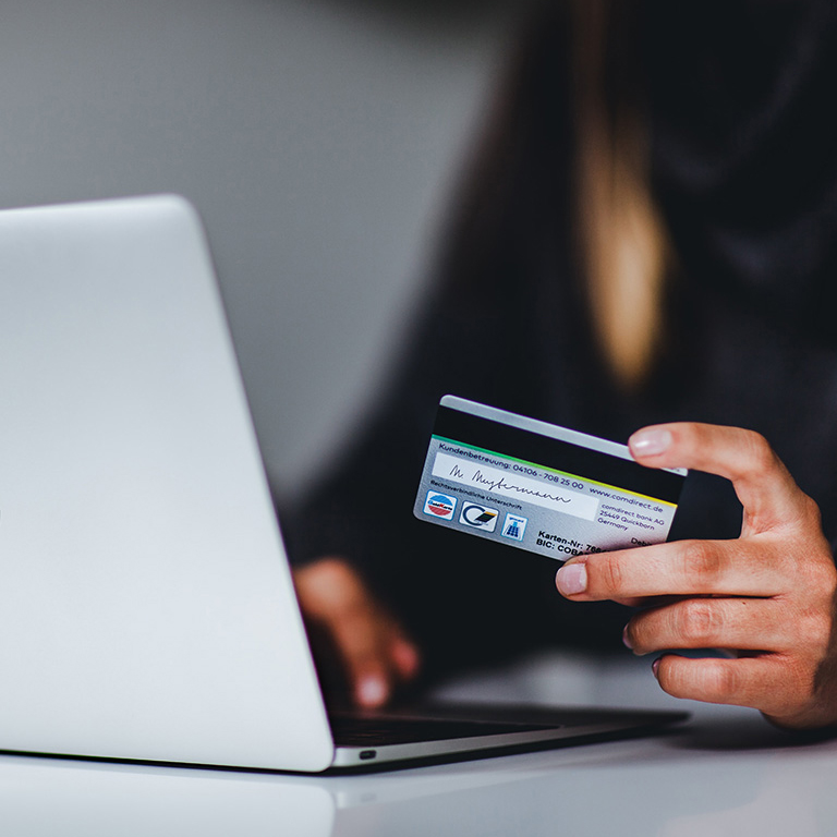 A person holding a debit card while working on a laptop.