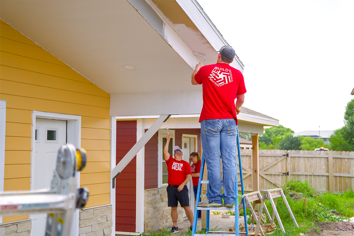 A man on a ladder painting the roof of a house.