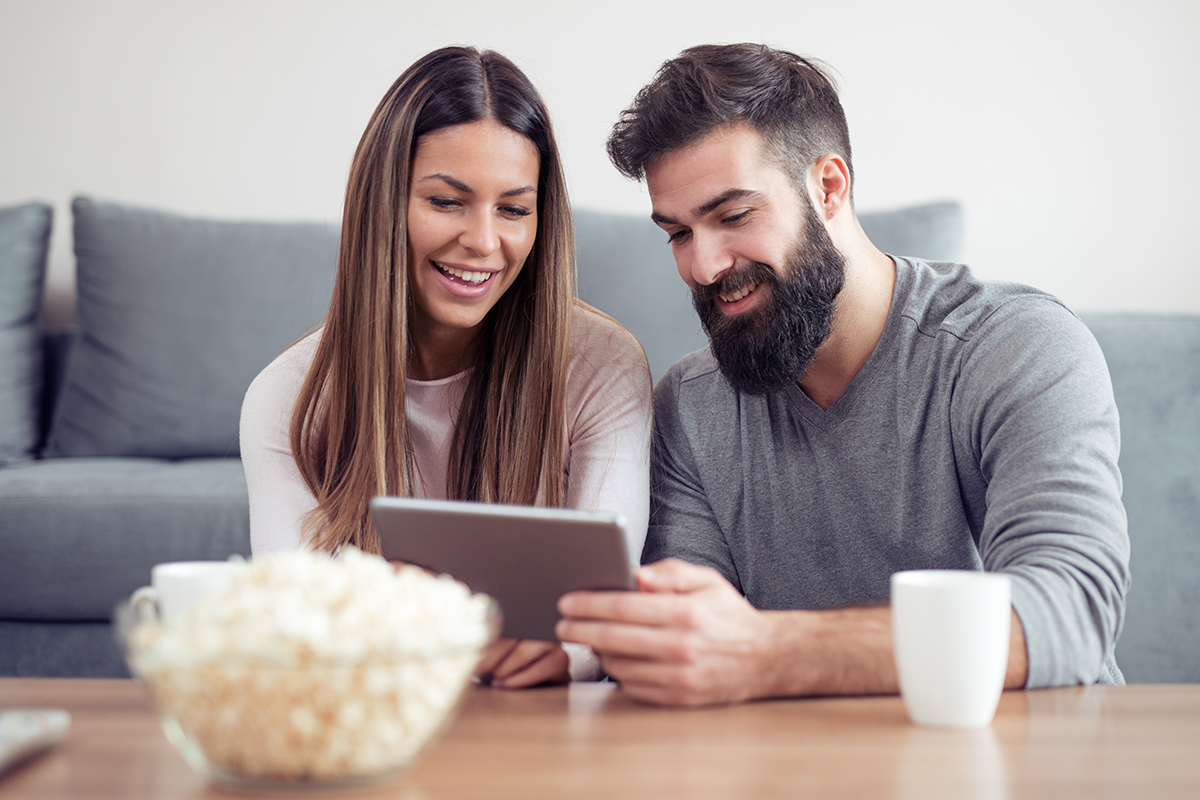 A young couple sitting in their living room looking at a tablet together.