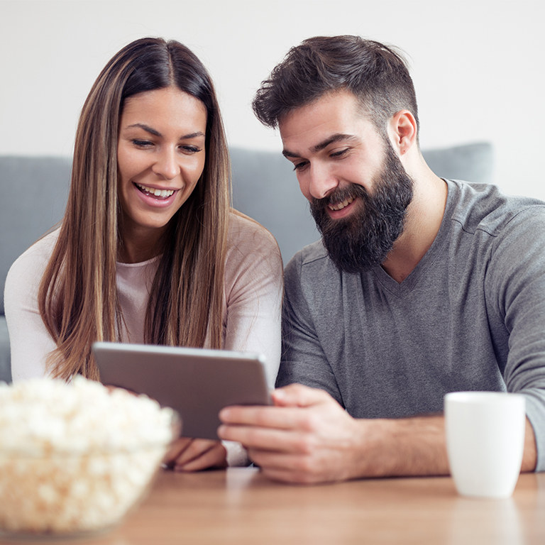 A young couple sitting in their living room looking at a tablet together.