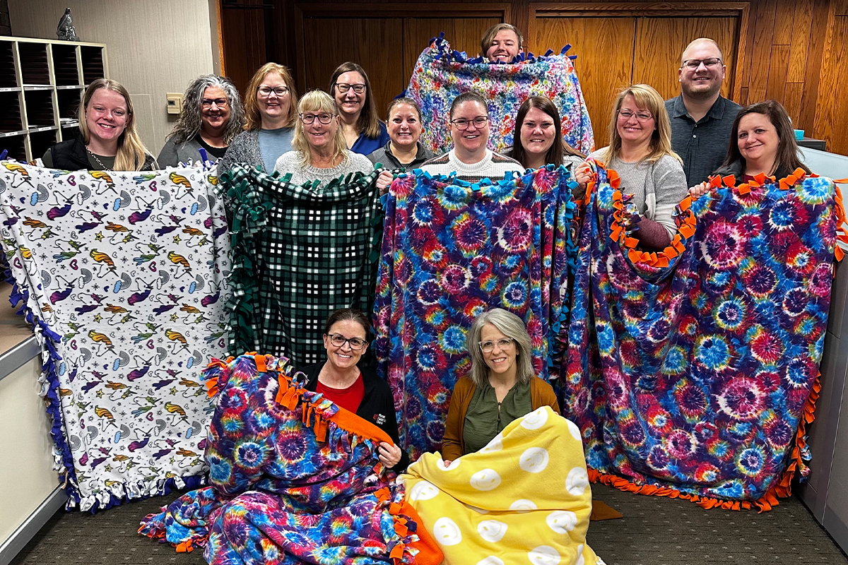 A group of people holding up fleece tie blankets.
