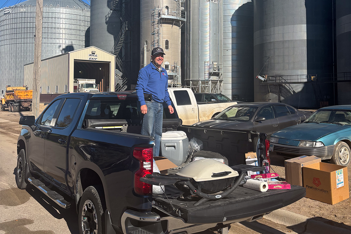 A man standing in the bed of a pickup with a grill and cooler.