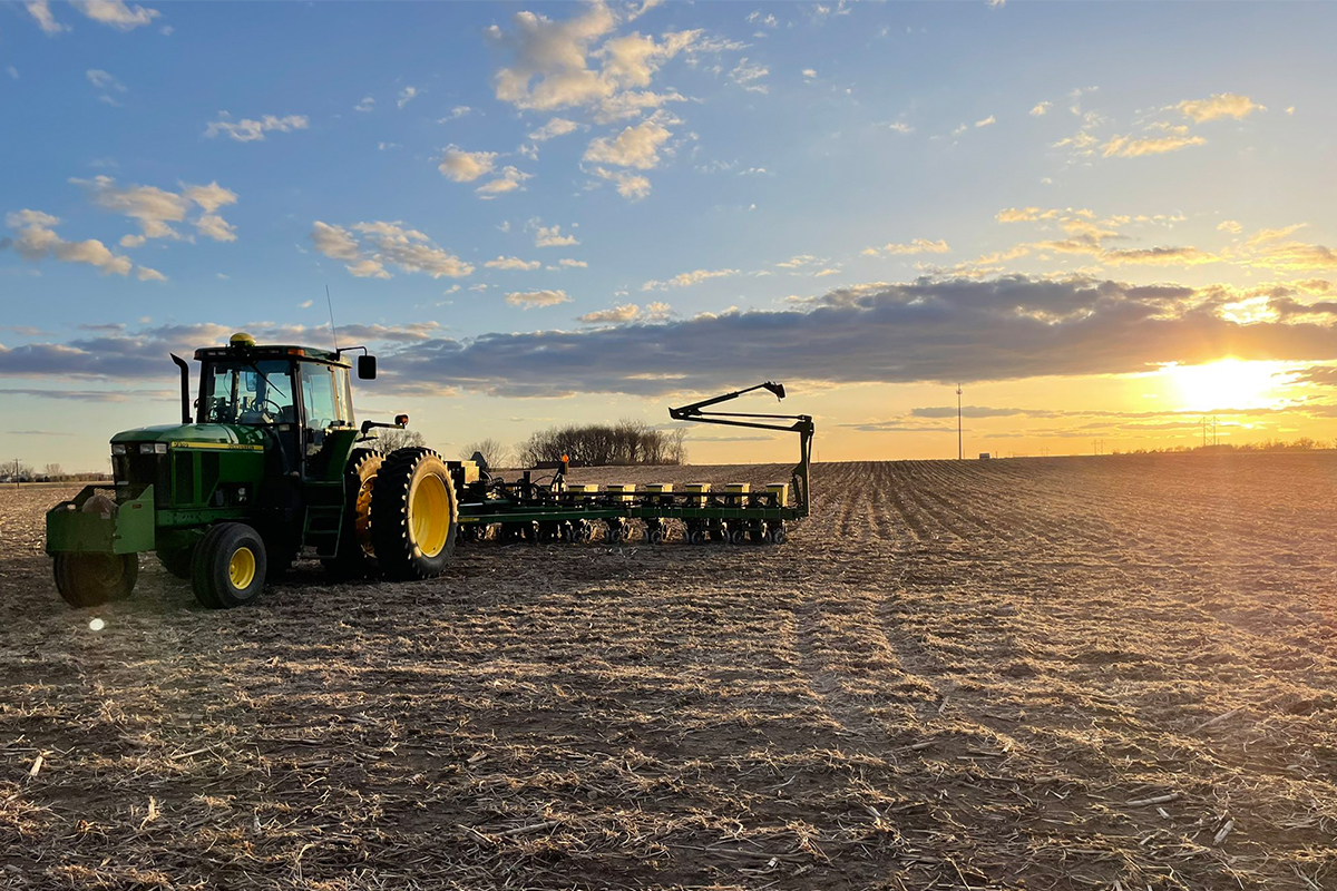 A tractor hooked up to a planter sitting in an empty field.