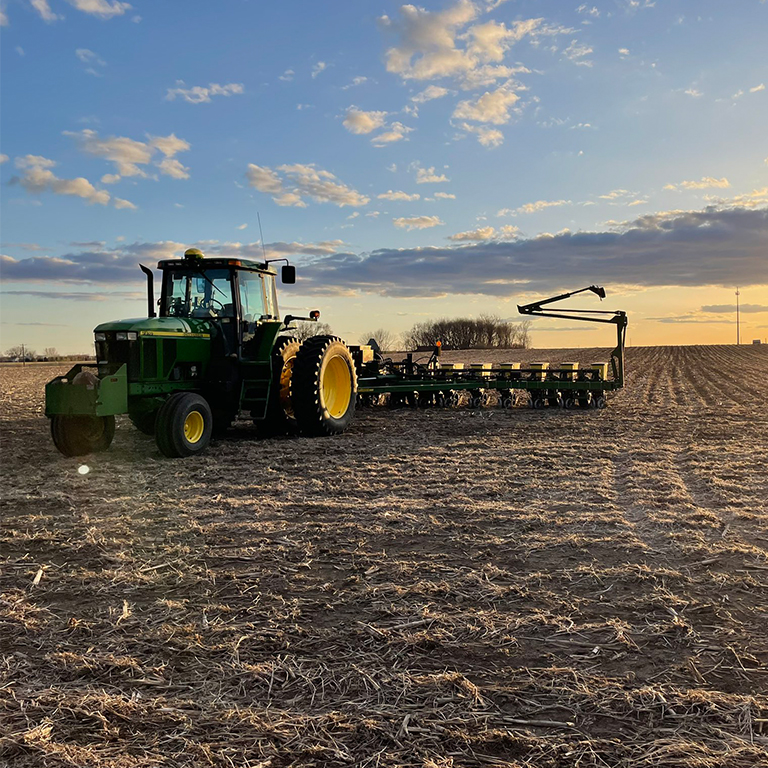 A tractor hooked up to a planter sitting in an empty field.
