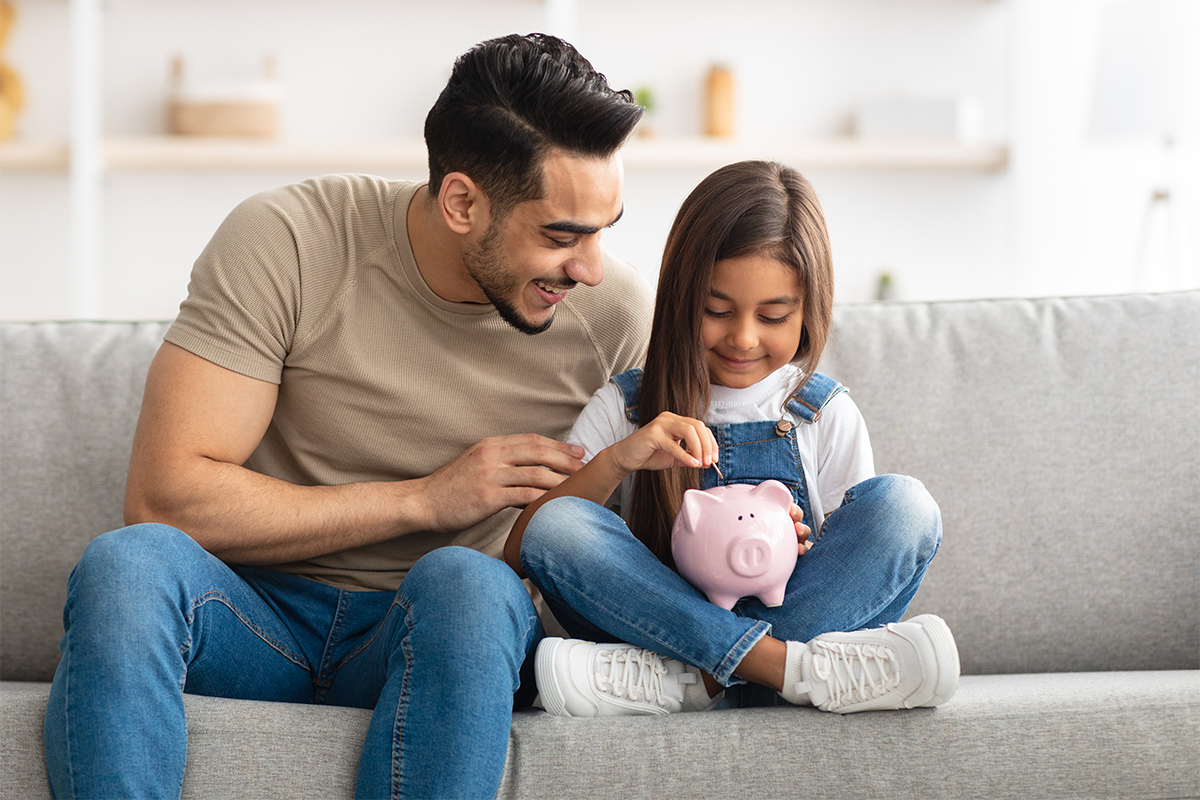 A father and daughter dropping coins into a piggy bank.