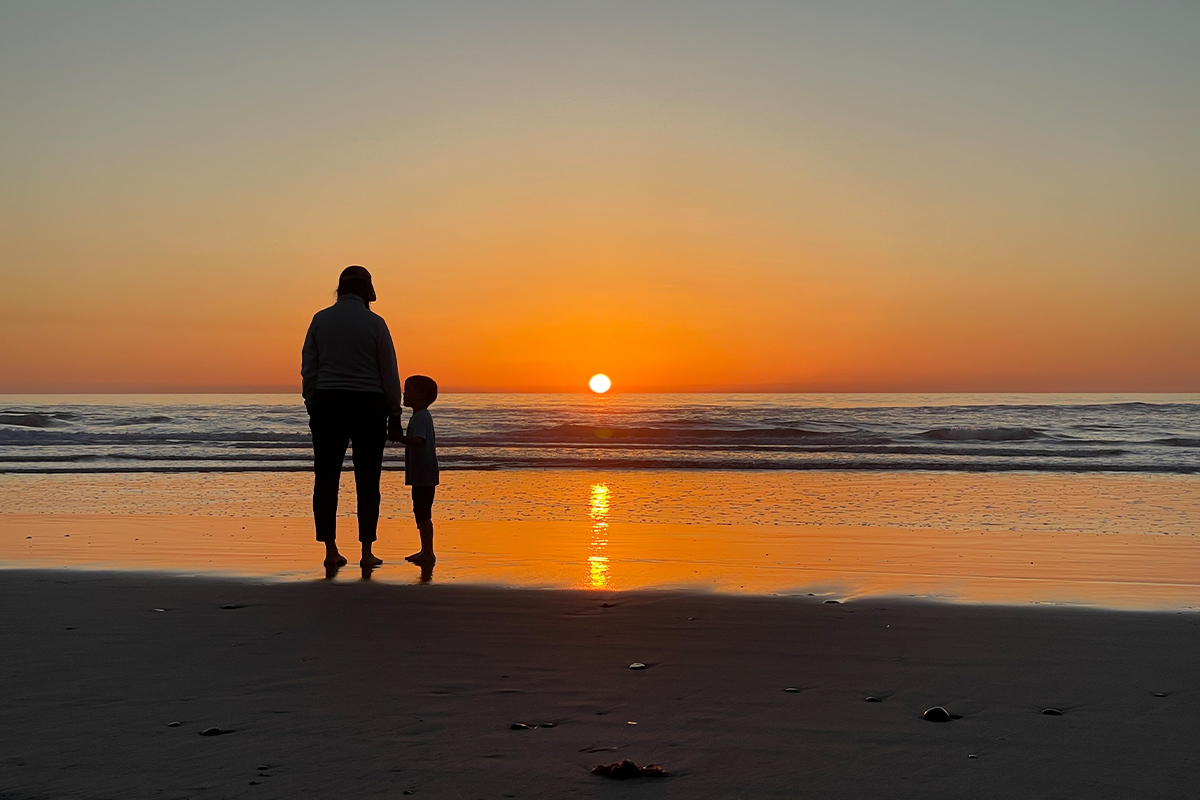 A mother and child standing on the beach at sunset.