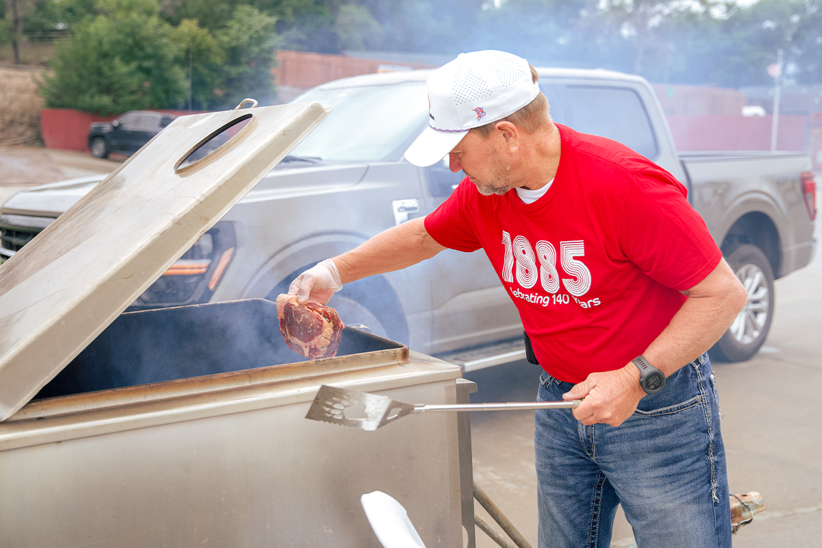 A man dropping steaks onto a grill.