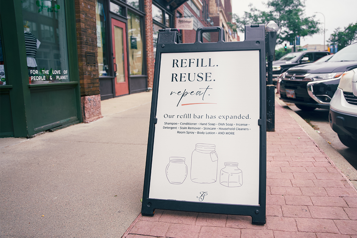 A sidewalk sign that reads, "Refill. Reuse. Repeat. Our refill bar has expanded."